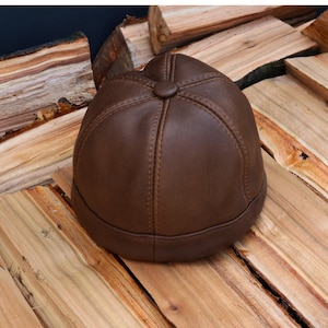 Puede incluir: Una gorra de béisbol de cuero marrón con una corona redonda y un diseño de costura.