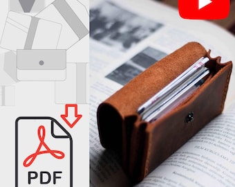 May include: A brown leather wallet with a snap closure, open to reveal multiple cards inside. The wallet is lying on a book with text in a foreign language.