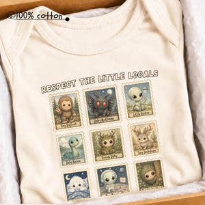 May include: A natural-colored baby bodysuit made of 100% cotton featuring a graphic print with the text "RESPECT THE LITTLE LOCALS" and nine postage stamp-style illustrations of various mythical creatures including Bigfoot, Mothman, and an alien.