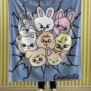May include: A blue fleece blanket with a cartoon design featuring a group of animals with the text "SKZOO" and "Charlotte" printed on it.