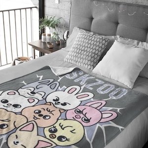 May include: A gray fleece blanket with a cartoon design of various animals with the word "SKZOO" printed on it.