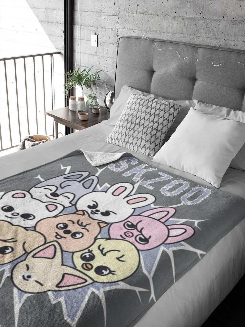 May include: A gray fleece blanket with a cartoon design of various animals with the word "SKZOO" printed on it.