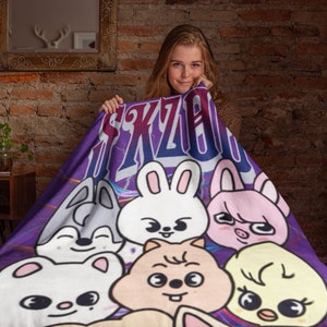 Puede incluir: Manta morada y azul con un estampado gr&aacute;fico de animales de dibujos animados y el texto "SKZOO".