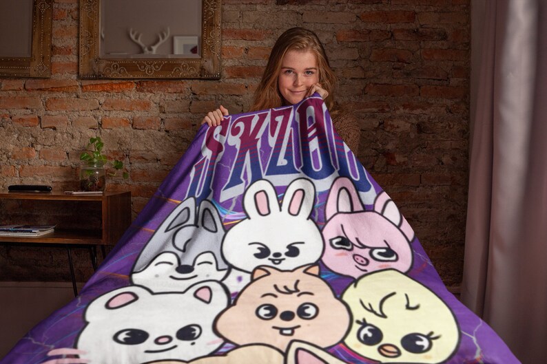 Puede incluir: Manta morada y azul con un estampado gr&aacute;fico de animales de dibujos animados y el texto "SKZOO".
