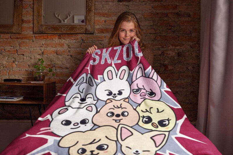 May include: A red and gray fleece blanket with a cartoon design featuring a variety of animals, including a rabbit, a pig, a wolf, a dog, and a bird. The blanket has the text "SKZOO" printed on it.