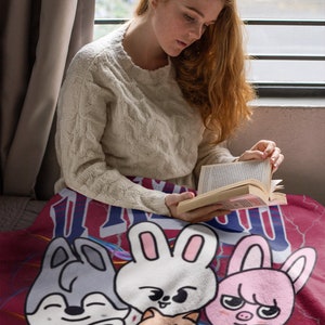 Puede incluir: Una manta roja, blanca y azul con un dise&ntilde;o de dibujos animados de varios animales, incluyendo un conejo, un gato, un perro, un cerdo y un pollo. Todos los animales sonr&iacute;en y tienen ojos grandes.