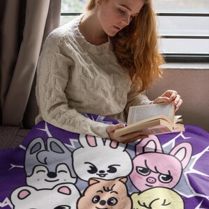 May include: A purple fleece blanket with a cartoon design featuring various animals with smiling faces. The animals include a rabbit, a pig, a bear, a bird, and a dog. The blanket is soft and cozy, perfect for snuggling up on the couch.