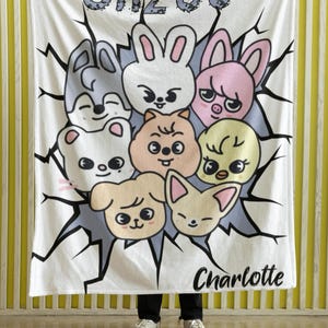 May include: White fleece blanket with a cartoon design featuring a group of animals with the text "SKZOO" and "Charlotte" printed on it.