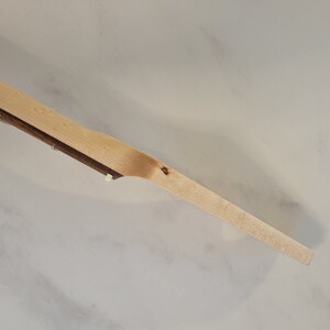 May include: A wooden paddle with a light brown finish. The paddle has a long, slender handle and a wider, flat blade. The wood grain is visible. The paddle is likely used for cooking or serving.