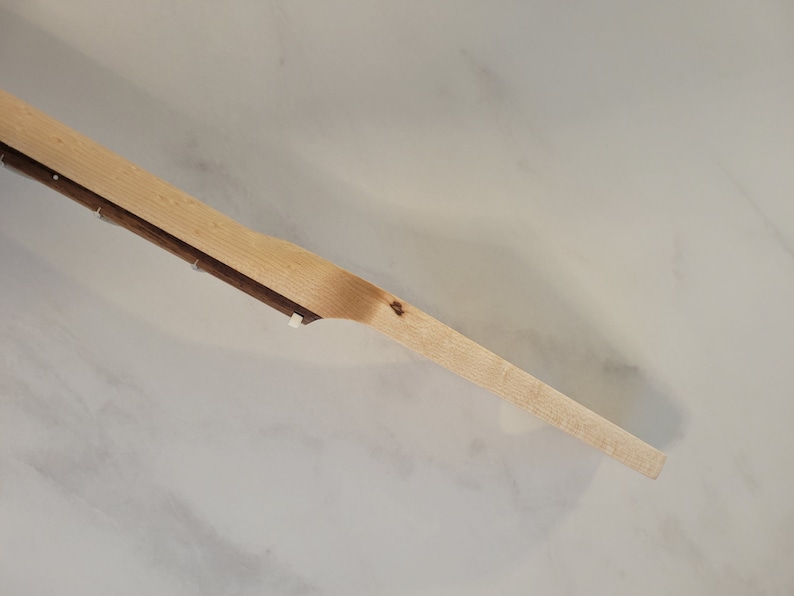 May include: A wooden paddle with a light brown finish. The paddle has a long, slender handle and a wider, flat blade. The wood grain is visible. The paddle is likely used for cooking or serving.