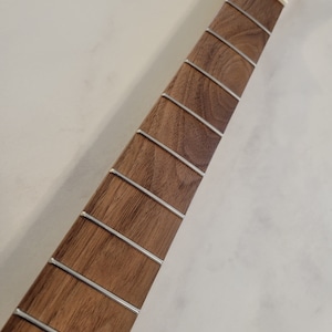May include: Close-up of a guitar neck with a dark brown fretboard and silver frets. The headstock is unfinished, showing the natural wood grain. The neck is a musical instrument component.