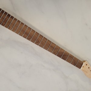 May include: A guitar neck with a dark brown fretboard and silver frets. The headstock is unfinished light wood with pre-drilled holes for tuning pegs. The neck is angled on a white surface.