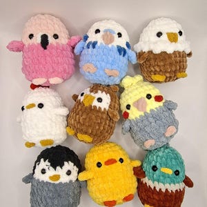 Puede incluir: Una colección de nueve juguetes de pájaros de peluche hechos a mano en varios colores. Los pájaros incluyen un loro rosa, un periquito azul, un búho marrón, un pollo blanco, un pollito amarillo, un pingüino gris y un pato verde azulado.