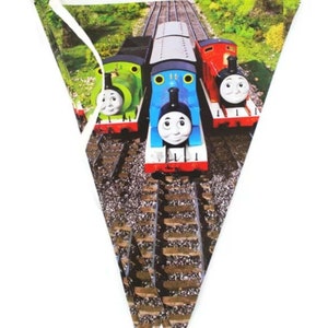 Könnte beinhalten: Ein dreieckiger Banner mit Thomas der Lokomotive als Motiv. Der Banner zeigt drei Züge: einen blauen Zug mit einem lächelnden Gesicht, einen grünen Zug mit einem lächelnden Gesicht und einen roten Zug mit einem lächelnden Gesicht. Die Züge befinden sich auf einem Gleis mit braunem Schotter.