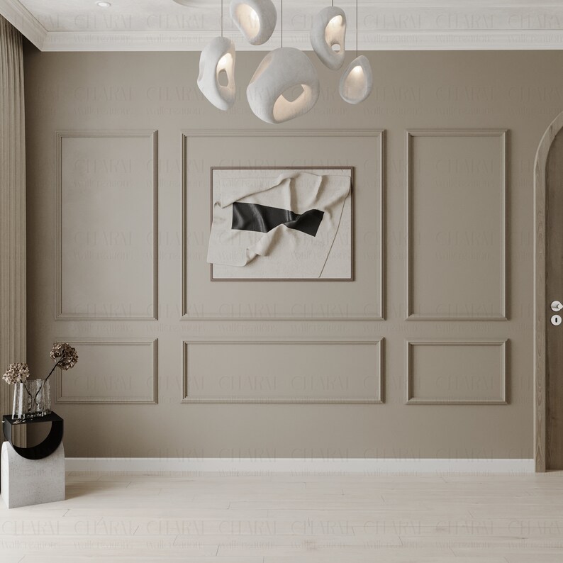 May include: A beige wall with white trim and a framed abstract art print with a black stripe. The wall is decorated with a modern light fixture with white, organic-shaped shades.