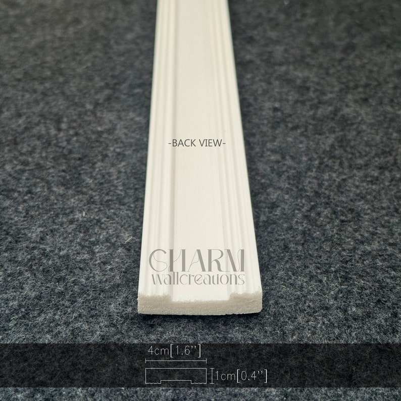 K&ouml;nnte beinhalten: Wei&szlig;e Polyurethan-Leiste mit dekorativem Design. Die Leiste ist 1,6 Zoll breit und 0,4 Zoll dick. Die R&uuml;ckseite der Leiste ist im Bild zu sehen. Der Text "CHARM wallcreations" ist auf die Leiste gedruckt.