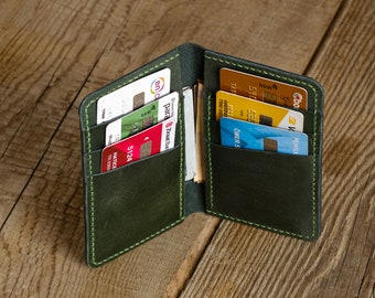 May include: Open, dark green leather wallet with multiple card slots. The wallet is filled with various credit cards and some cash. The stitching is a contrasting light green color. The wallet is open, displaying its contents.