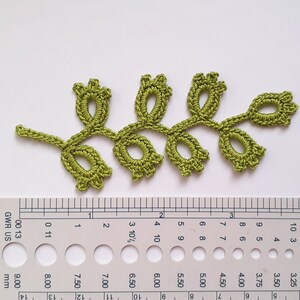 May include: A handmade, olive green crochet leaf with a delicate floral design. The leaf measures approximately 4 inches in length. The intricate details of the crochet work are visible, showcasing the craftsmanship. This item is perfect for embellishing clothing or craft projects.