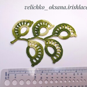 May include: A green and white crocheted leaf motif with a delicate, lacy design. The motif is approximately 4 inches wide and 3 inches tall.