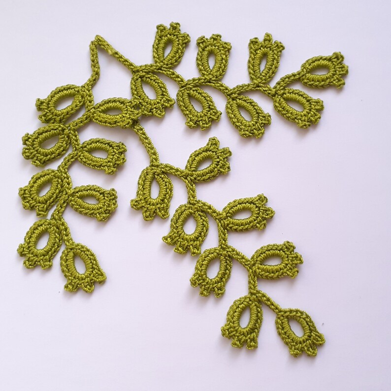 May include: A handmade, olive green crochet leaf design. The delicate, openwork leaves are arranged in a branching pattern. The crochet work is detailed, with each leaf having a distinct shape. The design is suitable for various craft projects.
