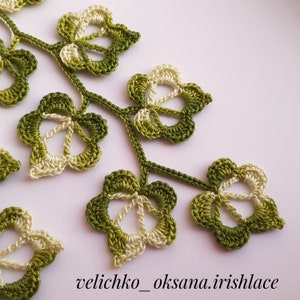 May include: Close-up of a crocheted green and white leaf design. The leaves are connected by a stem and have a delicate, intricate pattern.