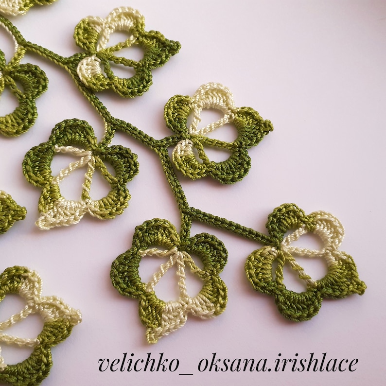 May include: Close-up of a crocheted green and white leaf design. The leaves are connected by a stem and have a delicate, intricate pattern.