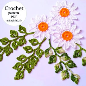 Op de afbeelding: Haakpatroon PDF in het Engels (VS) voor het maken van witte madeliefjes met oranje centra en groene bladeren.