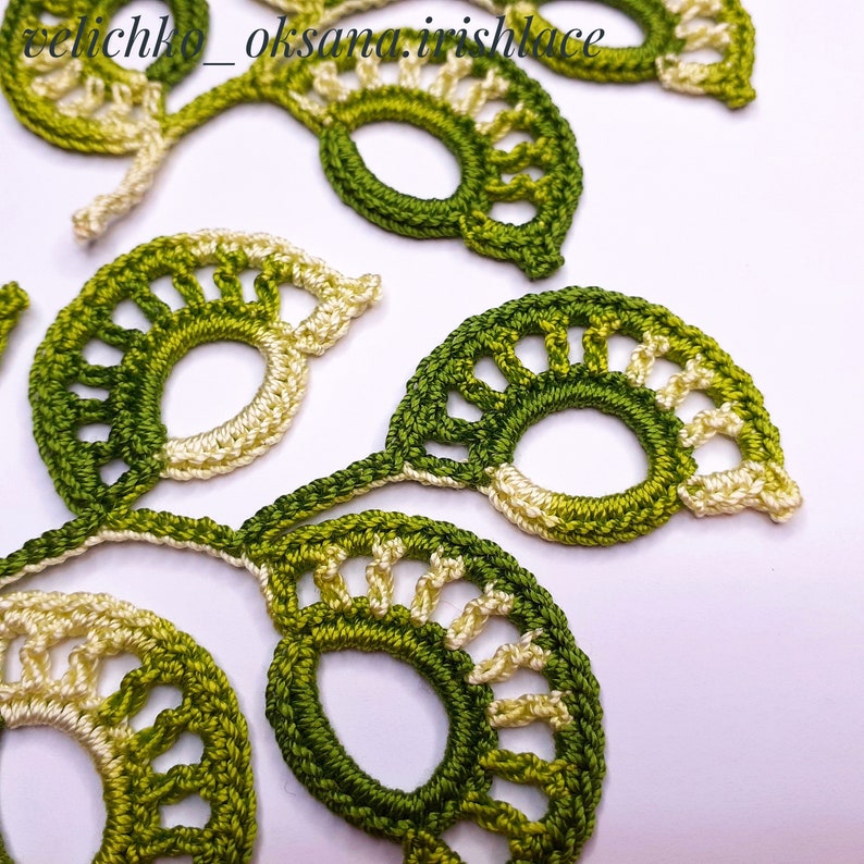 May include: A close-up of green and cream crocheted lace motifs with a circular design. The motifs are connected together to form a larger piece of lace.