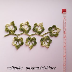 May include: A green and white crocheted leaf garland with a measuring tape in the background. The garland is about 6 inches long.