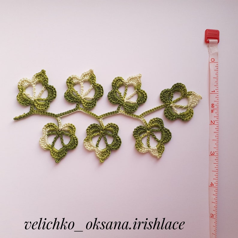 May include: A green and white crocheted leaf garland with a measuring tape in the background. The garland is about 6 inches long.