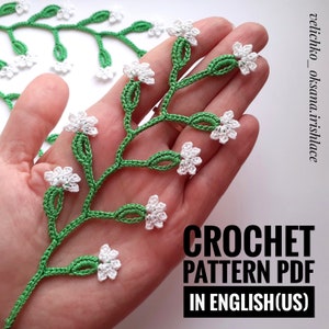 May include: A crochet pattern for a delicate white flower sprig with green leaves. The pattern is available as a PDF download in English (US).