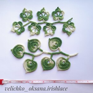 May include: Two crocheted green and white leaf garlands. The top garland has five star-shaped leaves and the bottom garland has five heart-shaped leaves. The garlands are approximately 7 inches long.
