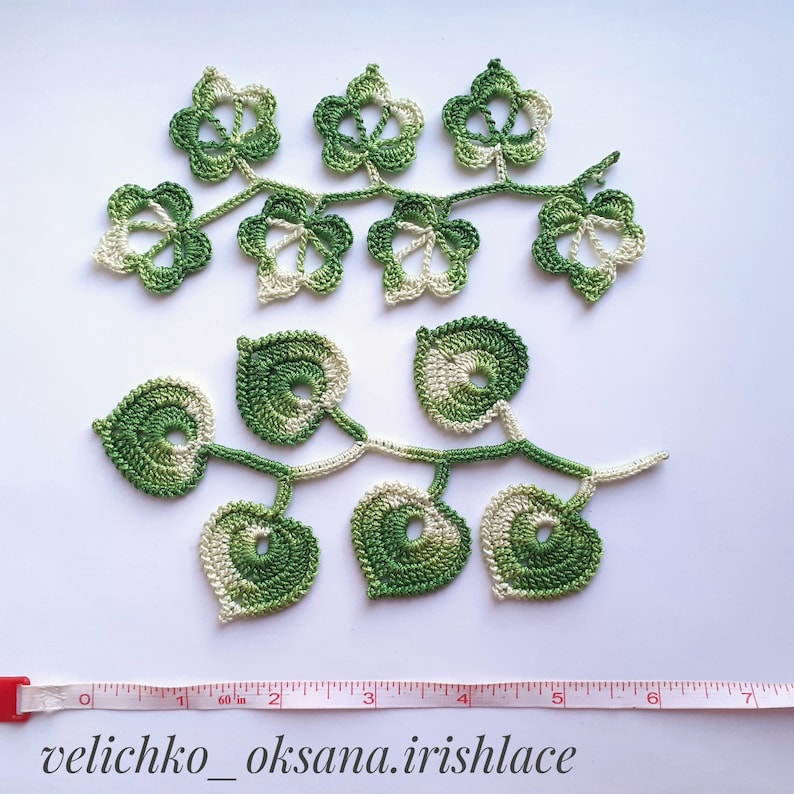 May include: Two crocheted green and white leaf garlands. The top garland has five star-shaped leaves and the bottom garland has five heart-shaped leaves. The garlands are approximately 7 inches long.