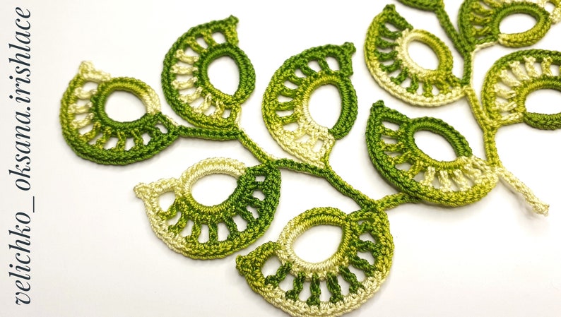 May include: A crocheted green and cream leaf motif with a delicate openwork design. The motif is made up of several smaller leaves connected together.