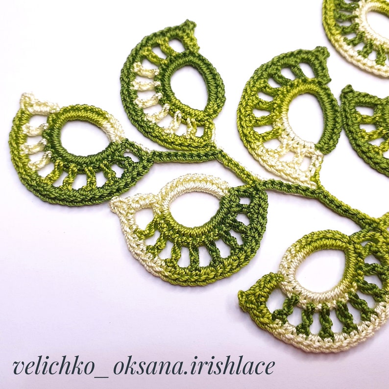 May include: A close-up of a crocheted green and white leaf design. The leaves are connected by a stem and have a delicate, lacy appearance.