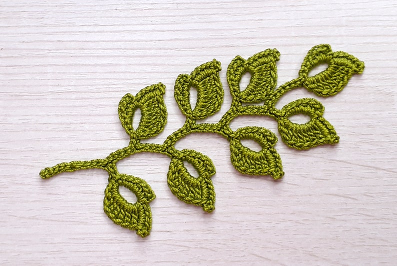 K&ouml;nnte beinhalten: Ein gr&uuml;ner geh&auml;kelter Bl&auml;tterzweig mit einem filigranen Design. Der Zweig hat mehrere Bl&auml;tter mit durchbrochenen Details.
