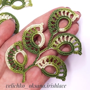 May include: A crocheted green and cream leaf motif with a delicate openwork design. The leaf is made with a combination of single crochet and double crochet stitches.