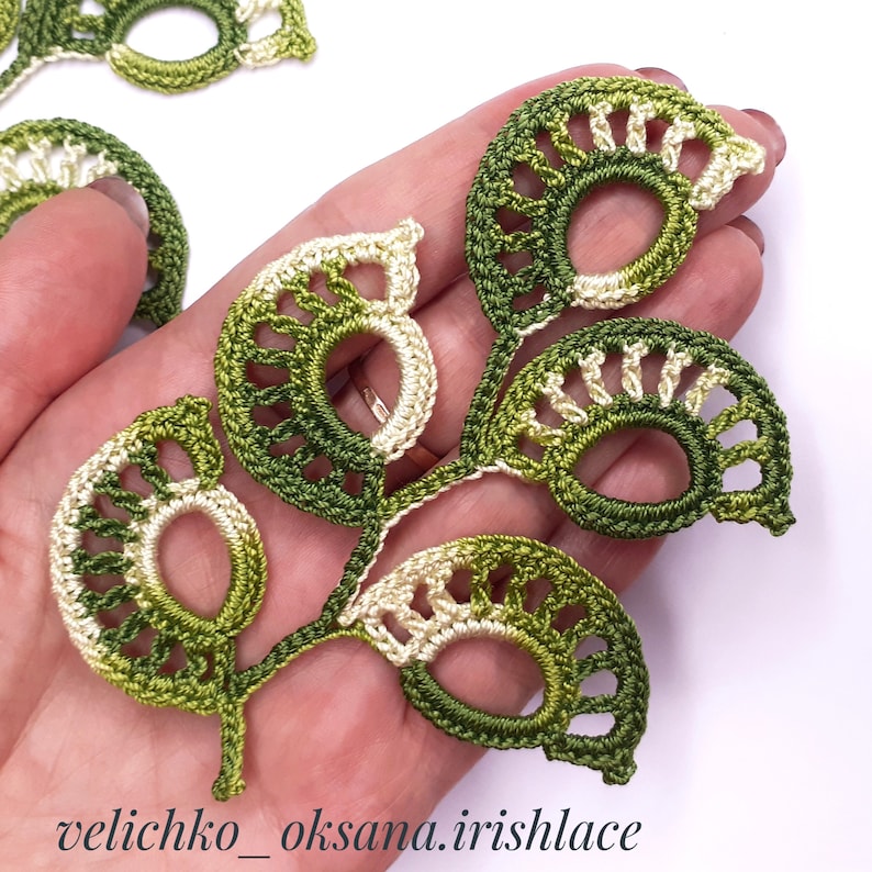 May include: A crocheted green and cream leaf motif with a delicate openwork design. The leaf is made with a combination of single crochet and double crochet stitches.