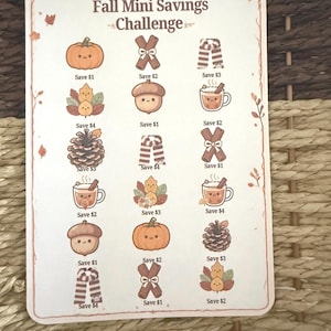 May include: A rectangular Fall Mini Savings Challenge card featuring a grid of cute autumn-themed illustrations including pumpkins, acorns, pinecones, scarves, and mugs. Each icon is labeled with a dollar amount to save, totaling $43.