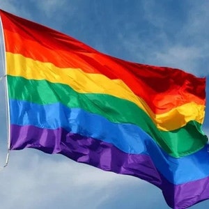 May include: A rainbow pride flag waving in the wind against a blue sky with white clouds.