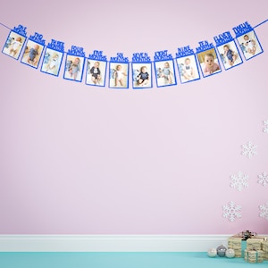 May include: A blue and white baby monthly milestone banner with 12 photo frames. Each frame has a number and the word "months" printed on it. The banner is hanging on a pink wall.