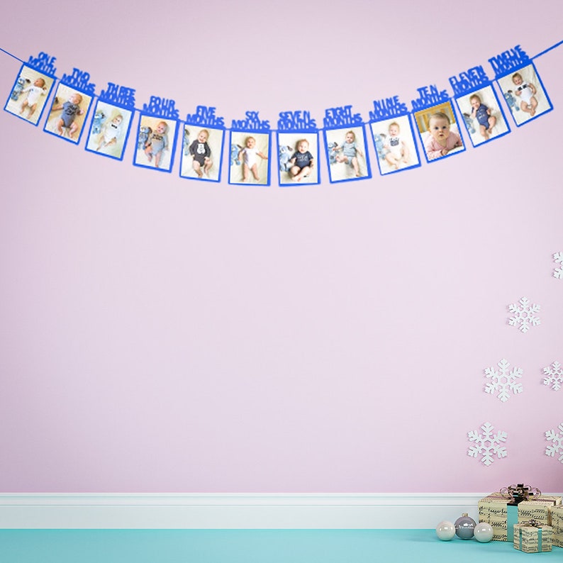 May include: A blue and white baby monthly milestone banner with 12 photo frames. Each frame has a number and the word "months" printed on it. The banner is hanging on a pink wall.