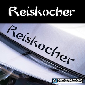Może przedstawiać: Czarno-biała naklejka z napisem "Reiskocher" napisanym stylizowanym fontem. Naklejka jest przyklejona do tylnej części srebrnego samochodu.