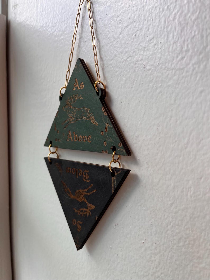 May include: A hanging wall decoration consisting of two triangular wooden plaques connected by gold-colored metal jump rings and a chain. The top green plaque features a deer illustration and the text "As Above," while the bottom black plaque features a deer illustration and the text "So Below."