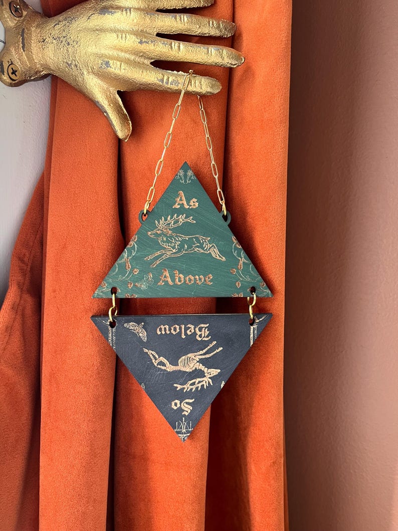 May include: A two-part hanging wall ornament featuring triangular wooden panels connected by gold chains. The top green panel displays a leaping deer and the text As Above, while the bottom dark panel shows a deer skeleton and the text So Below.