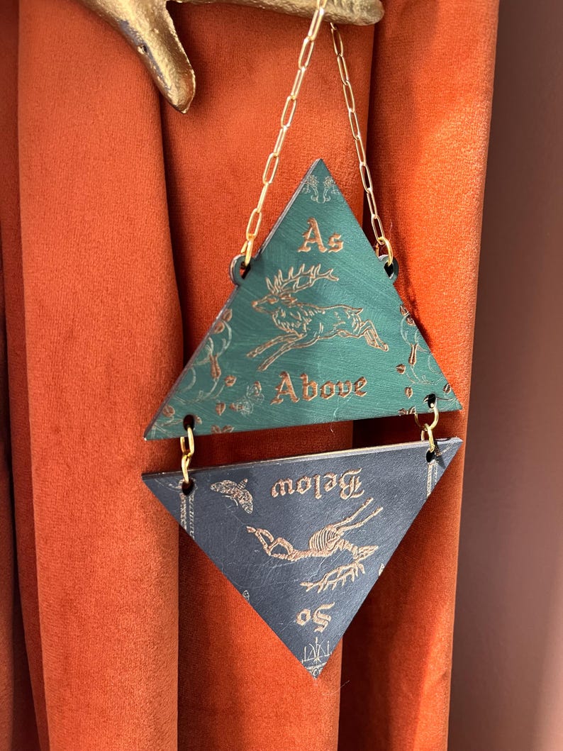 May include: A hanging wall ornament consisting of two triangular wooden panels connected by gold-colored metal chains. The top green panel features a gold deer illustration and the text As Above. The bottom dark panel features a gold deer skeleton and the text So Below.