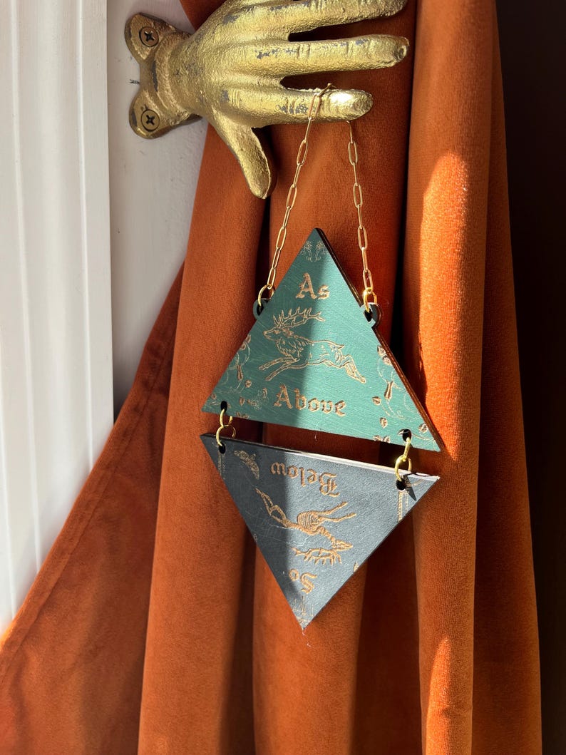 May include: A hanging wall ornament consisting of two triangular wooden plaques connected by gold-colored metal chains. The top green plaque features a gold deer illustration and the text "As Above," while the bottom black plaque features a gold deer skeleton illustration and the text "So Below."