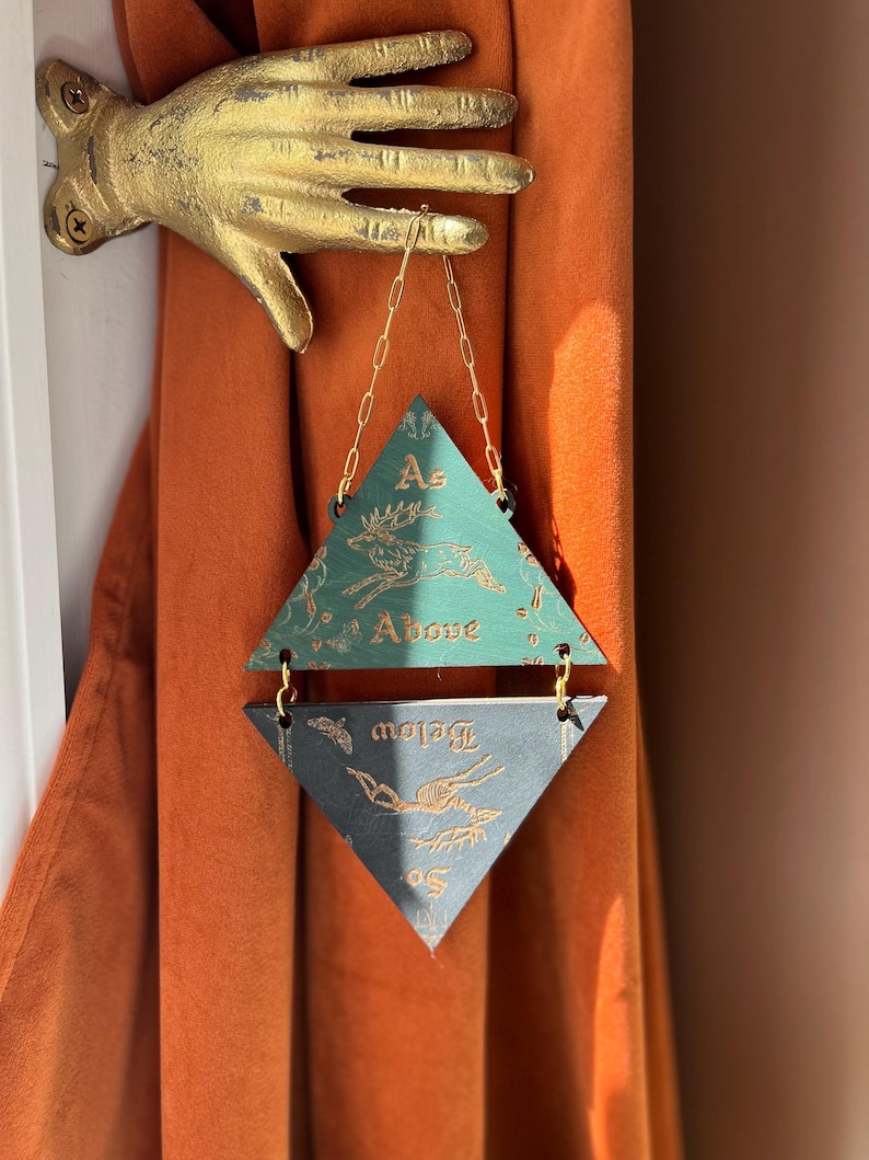 May include: A gold-colored metal hand wall mount holding a hanging ornament composed of two stacked triangles connected by gold chains. The top green triangle features a deer illustration and the text As Above, while the bottom dark triangle shows a skeletal deer and the text So Below.