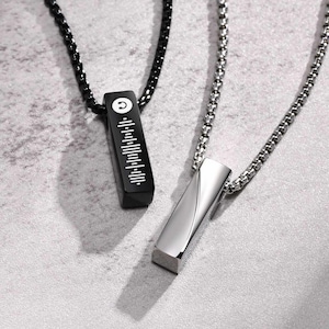 Pode incluir: Dois colares de prata com barras pendentes combinando. Uma barra é preta com uma nota musical e um código de barras, a outra é prateada e tem um design em espiral.