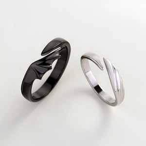 May include: A pair of matching rings with wing designs. One ring is black and the other is silver.